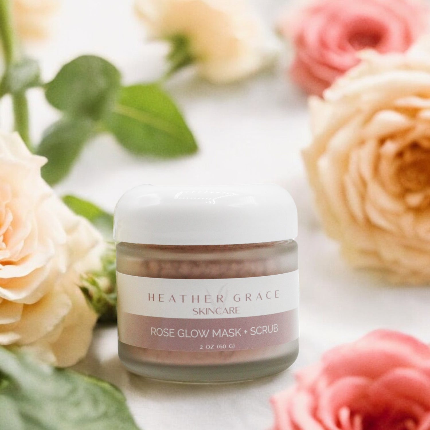 Close-up of Heather Grace Rose Glow Mask + Scrub in a white jar with a floral backdrop, emphasizing the product&